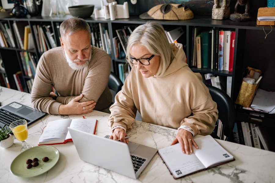 Senior couple reviewing notes and laptops together at a table